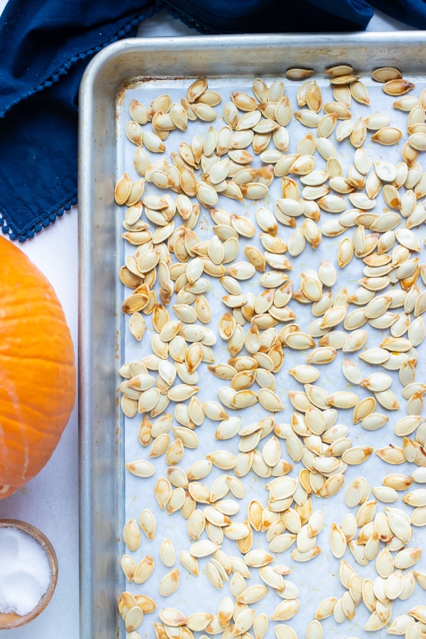 Seasoned pumpkin seeds are baked in the oven on a large baking sheet.