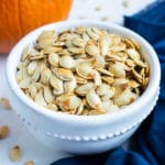 Pumpkin seeds are placed in a white bowl on the counter in this fall recipe.