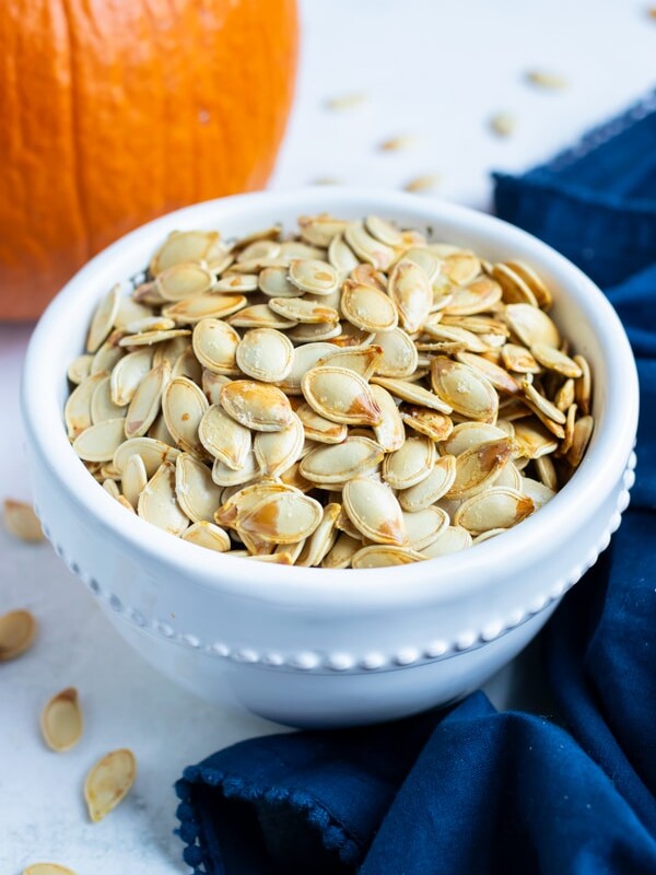 Pumpkin seeds are placed in a white bowl on the counter in this fall recipe.