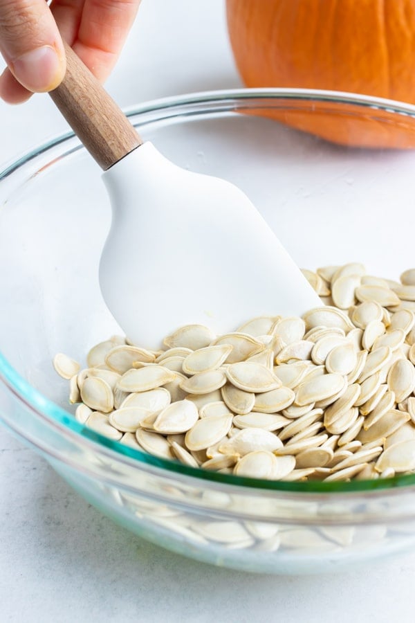 Oil or butter, pumpkin seeds, and seasonings are combined in a bowl and mixed.
