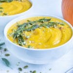 Vegetarian pumpkin soup made with coconut milk is served in a bowl on the counter.