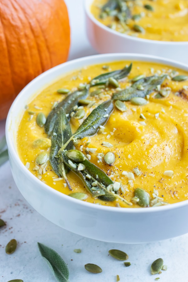 Pumpkin soup is topped with sage leaves and pumpkin seeds for an easy and stunning appetizer.