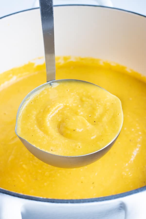 Creamy butternut squash soup being scooped up out of a pot.