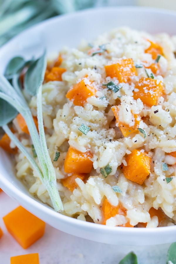 Smooth and creamy butternut squash risotto is served with fresh herbs and topped with parmesan cheese.