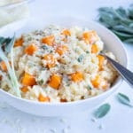 Homemade butternut squash risotto is served in a white bowl with a spoon.