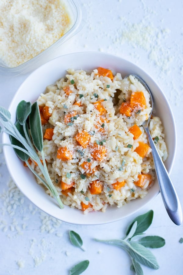 A bowl of butternut squash risotto is topped with sage and parmesan cheese.