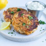 Homemade crab cakes are served on a white plate with fresh lemon and tartar sauce.