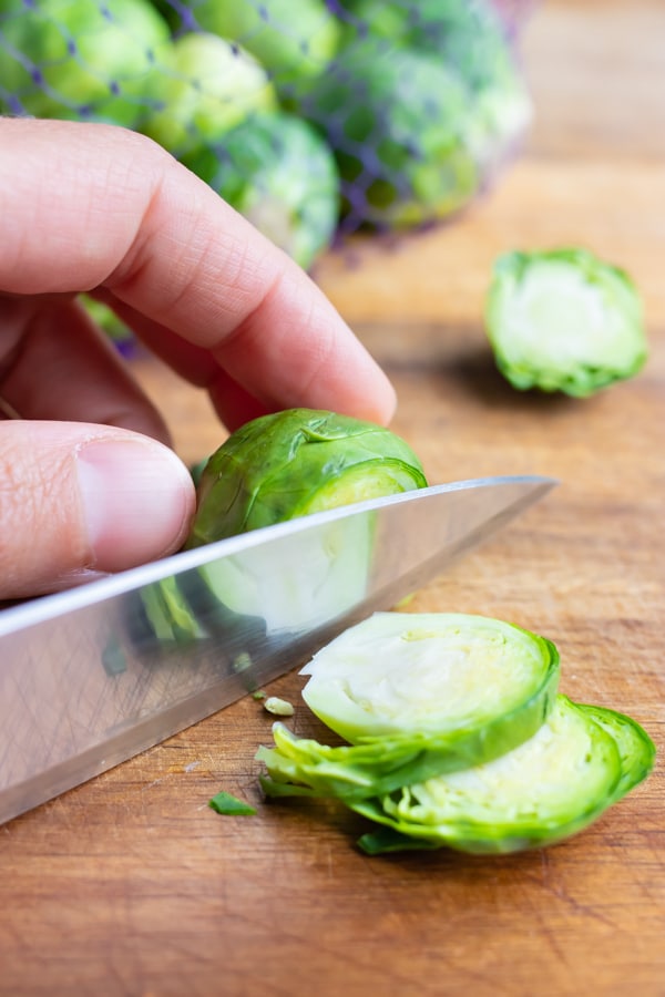 Raw brussels sprouts are chopped into thin slices on a cutting board.