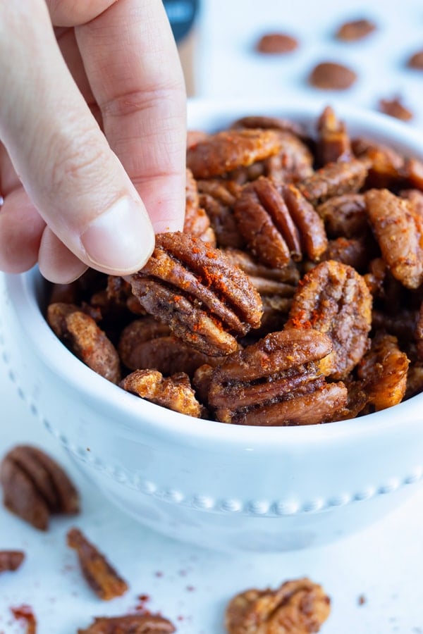 Pecans are toasted and snacked on from a white bowl.