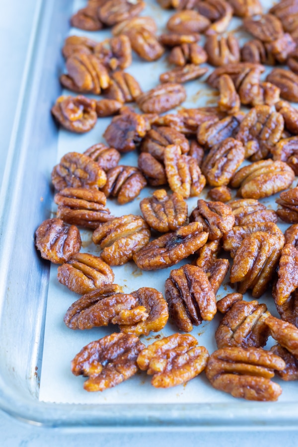 Spicy and sweet coated pecans are laid flat on a large baking sheet.