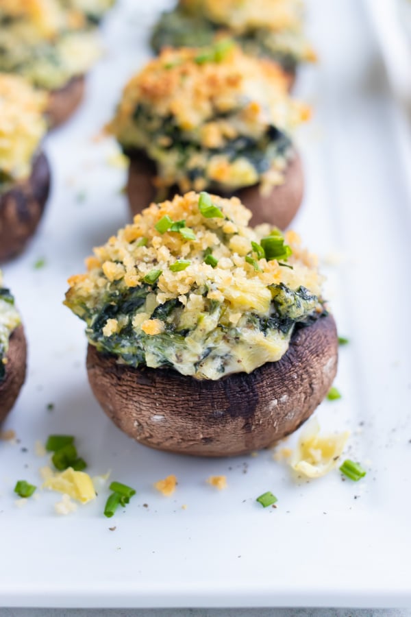 Vegetarian spinach stuffed mushrooms are lined up on a tray to be served at as an appetizer.