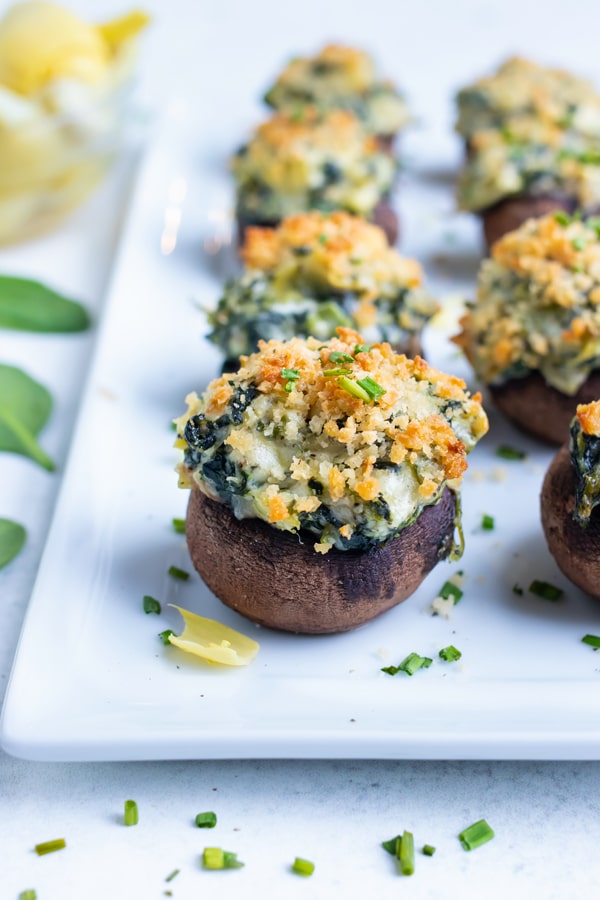 Low-carb spinach filled mushrooms are served on a white tray at a party.