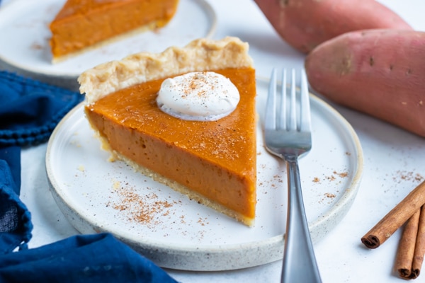 A slice of sweet potato pie is served on a white plate with a fork.