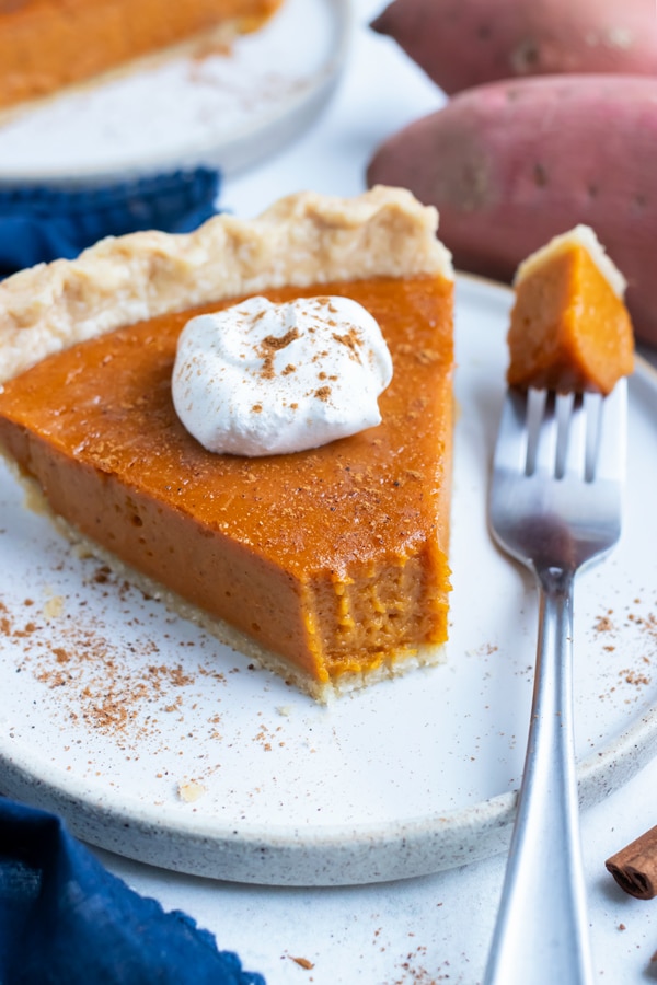 Sweet potato pie served on a plate with a dollop of whipped cream on top.