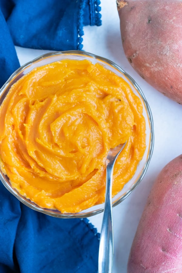 Easy sweet potato puree is in a glass bowl with a metal spoon.