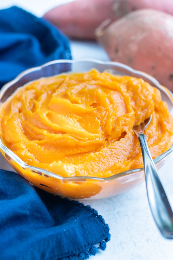 Sweet potato puree is in a glass bowl with a metal spoon on the counter.