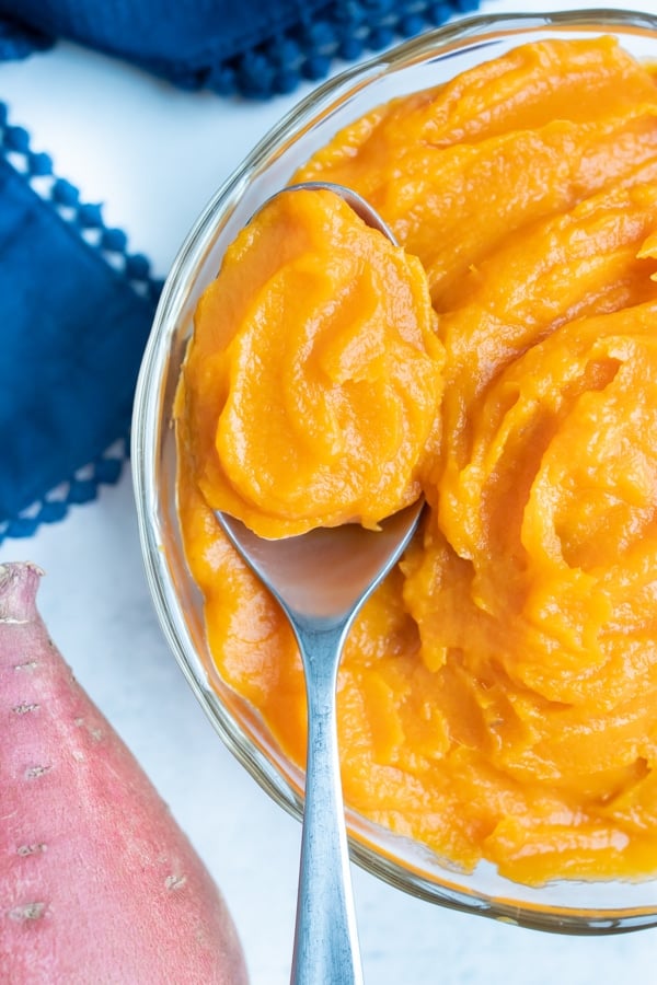 A spoon lifts out creamy homemade sweet potato puree for use in pies.