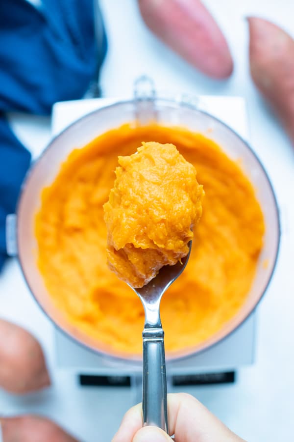 A spoon lifts the sweet potato puree out of the food processor.