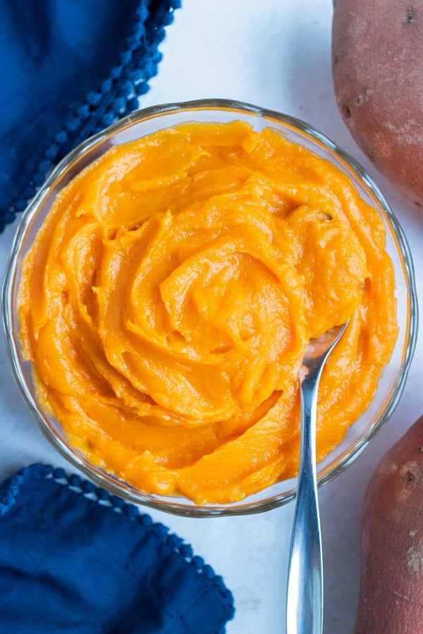 Easy sweet potato puree is placed in a glass bowl with a spoon for dishing.