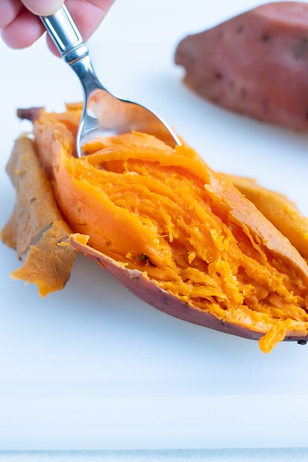 Inside of sweet potatoes is scooped out with a spoon in homemade puree recipe.