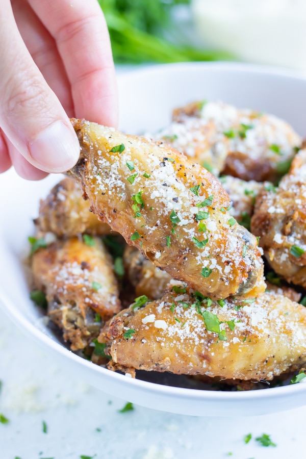Garlic air fryer chicken wings are lifted up out of a white bowl.
