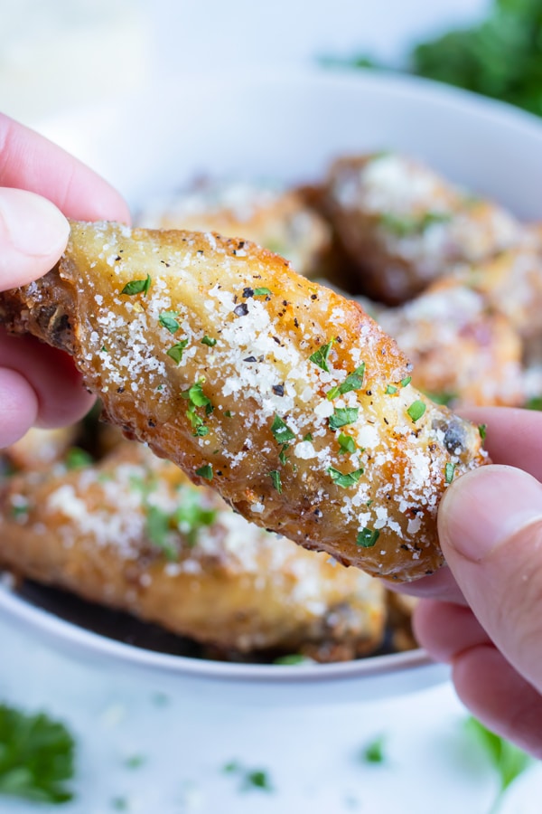 One chicken wing is held up by a hand.