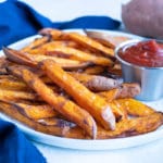 A plate of sweet potato fries are served at a meal with ketchup.