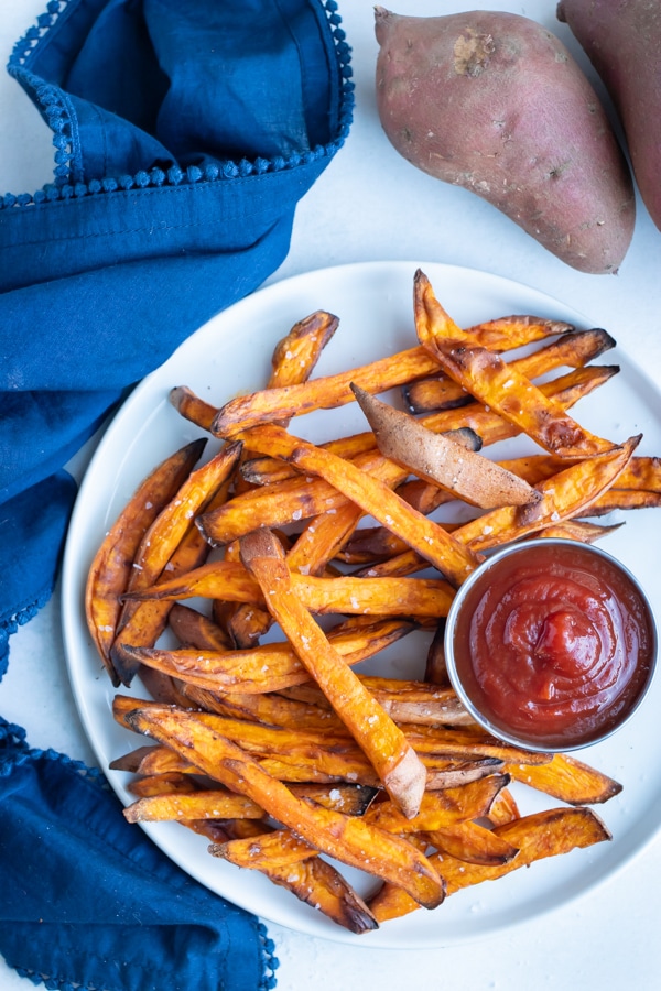 A plate of crispy sweet potato fries are served with ketchup for a side.