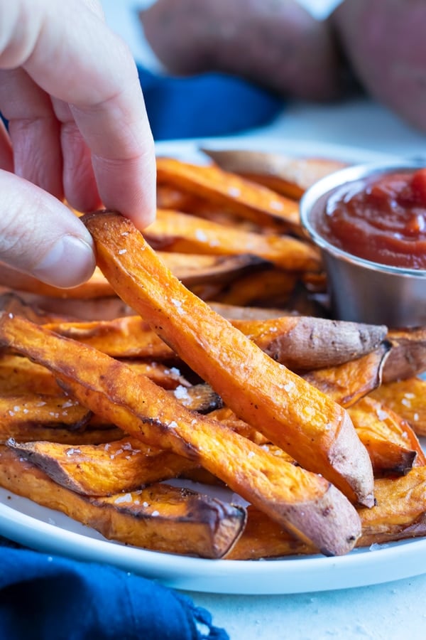 A sweet potato fry is lifted up by a hand for a healthy side.