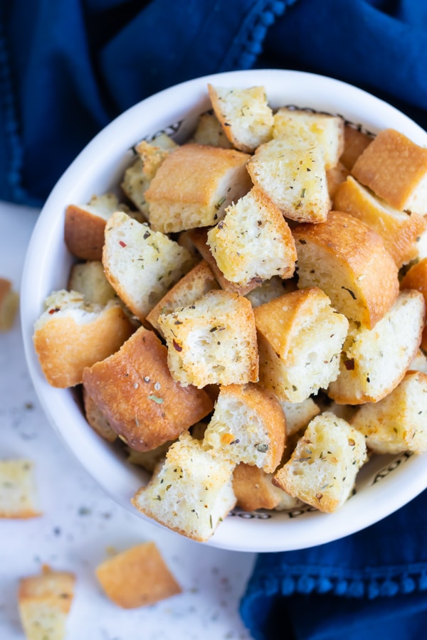 A white bowl is full of homemade croutons with a blue napkin.