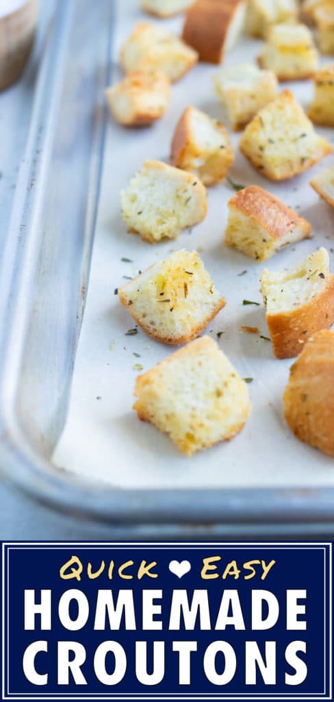 A close up pictures of herb and garlic homemade croutons on a baking sheet is shown.
