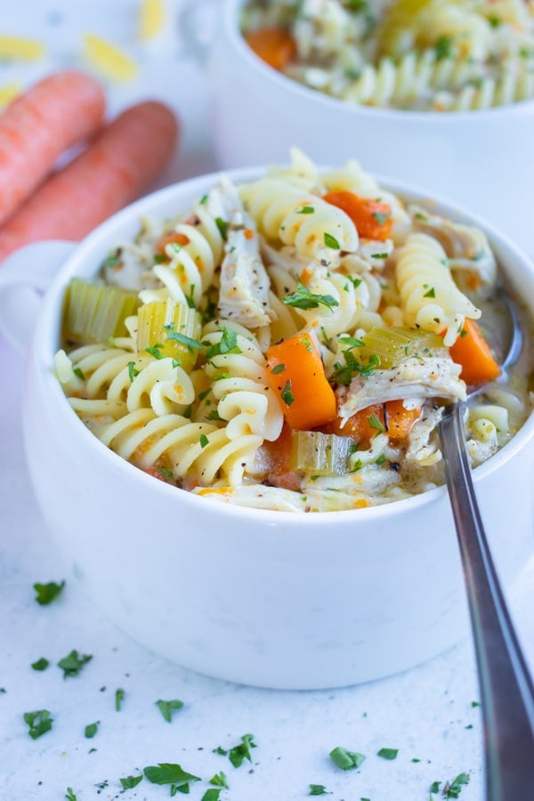 A white bowl is loaded with a healthy chicken noodle soup.