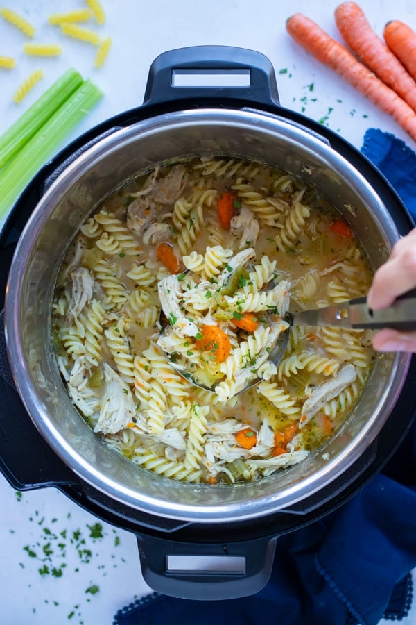 Healthy chicken noodle soup is stirred with a metal spoon in the instant pot.