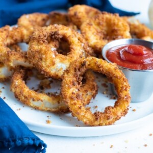 Crispy air fryer onion rings are served on a plate with ketchup.