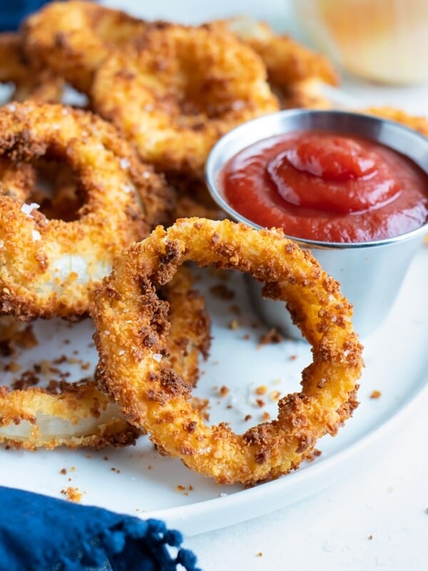 Ultra crispy onion rings are served as an appetizer on a white plate.