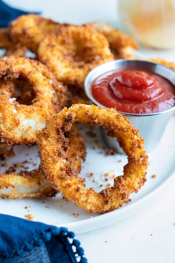 Air Fryer Onion Rings RECIPE served on a white plate with a side of dipping sauce.