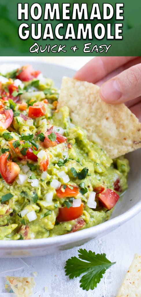 A tortilla chip being dipped into a healthy guacamole dip with tomatoes, onions, and cilantro.