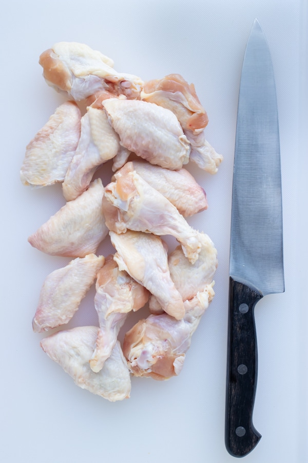 A knife is set beside a pile of cut chicken wings on the counter.