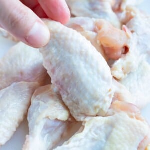 A wingette is lifted up by a hand out of a pile of cut chicken wings.