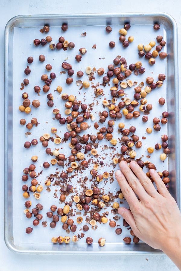 Toasted, golden hazelnuts are touched by a hand.