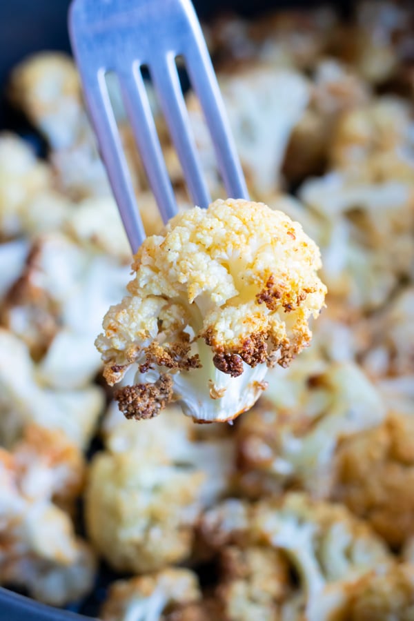 A piece of seasoned cauliflower is lifted up by a fork.