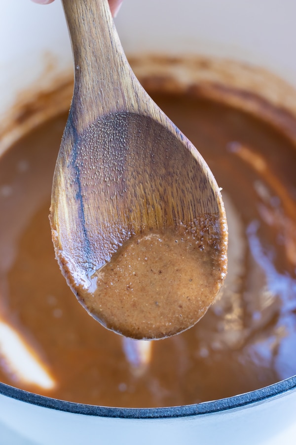 A wooden spoon is used to stir light brown roux.