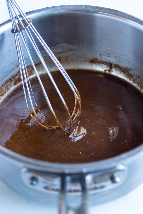 A whisk is used to stir a dark brown roux.