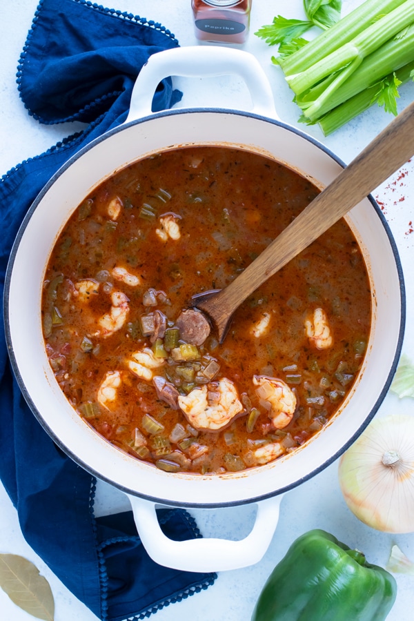 Louisiana gumbo is stirred in a large pot with a wooden spoon.