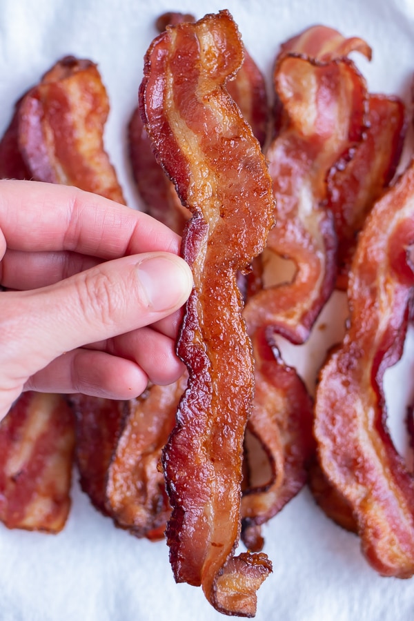 A slice of cooked bacon is lifted up by a hand.