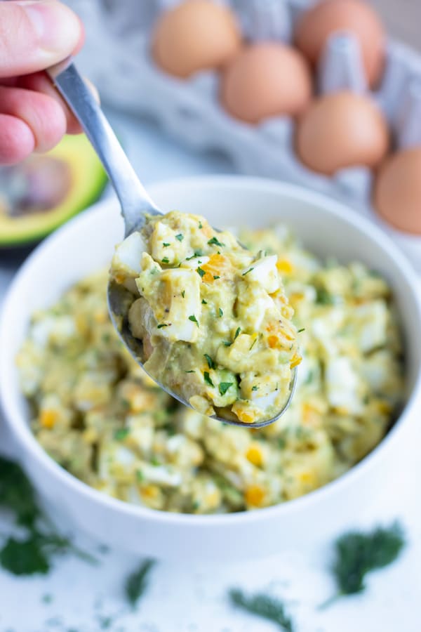 A spoon is lifted up full of avocado egg salad.