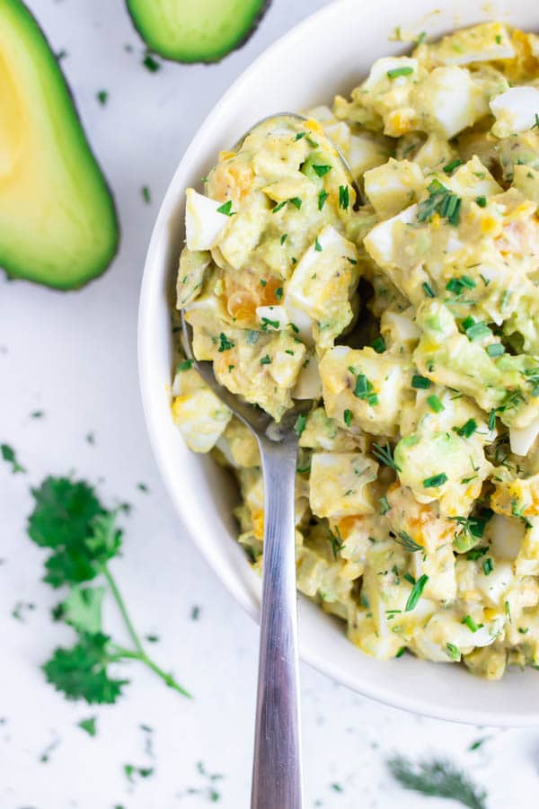 Healthy avocado egg salad is served in a bowl with a spoon.