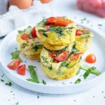 Tomato, spinach, and cheese egg muffins are stacked on a plate for breakfast.