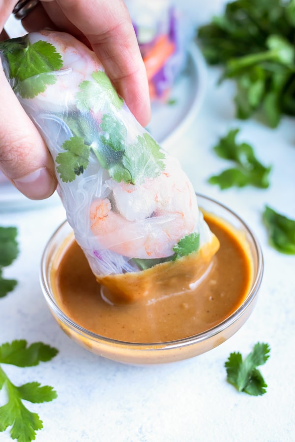 A spring roll is dipped into a homemade peanut sauce. 