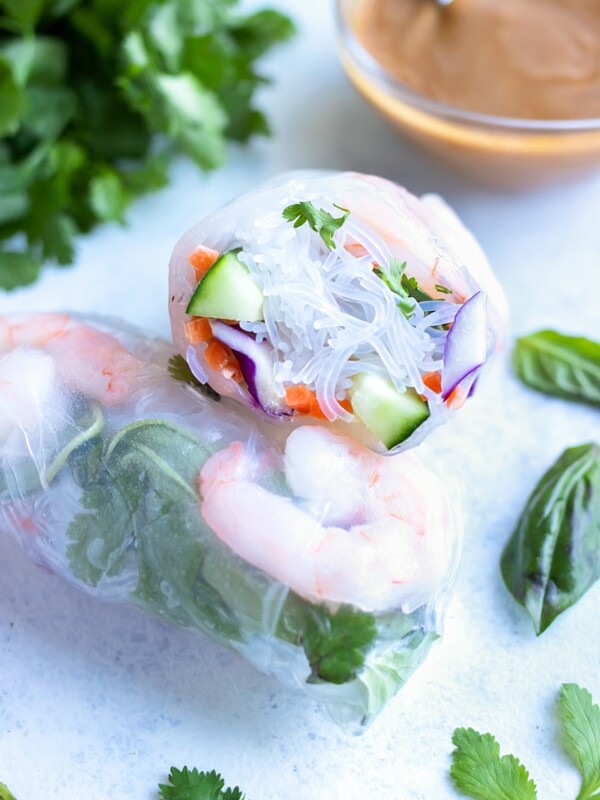 Fresh spring rolls are shown on the counter with herbs and a peanut sauce behind them.